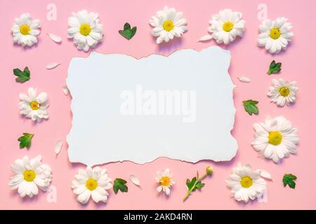 Composizione di fiori con crisantemo bianco fiori, foglie verdi petali di colore bianco e bianco carta Vuota elenco su sfondo rosa Foto Stock