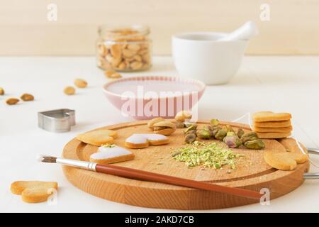 Preparare per il giorno di San Valentino. Iced piccante biscotti frollini nel cuore forme, abbellito con calce-lampone ghiaccio tritato e i pistacchi. La cottura wi Foto Stock