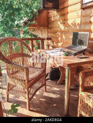 Posto di lavoro in un'area aperta nel giardino con mobili di vimini sotto l'uva. Un luogo per un libero professionista. Il concetto di lavoro libero. Foto Stock