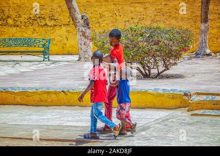 Isola di Goree, Senegal- 22 aprile 2019: ragazzi non identificato a piedi lungo una strada di sabbia in una piccola città e trasportare un tamburo di legno. Foto Stock