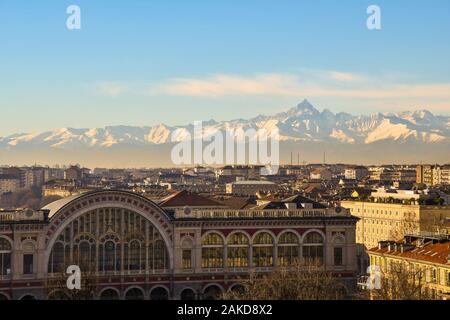Vista sui tetti di Torino con la cima della stazione ferroviaria di porta nuova e delle Alpi Cozie con la vetta del Monviso in una soleggiata giornata invernale, Piemonte, Italia Foto Stock