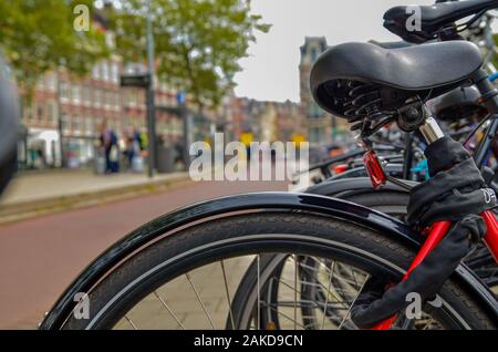 Amsterdam, Olanda, Agosto 2019.Un particolare punto di vista: dal telaio sfocata e la sella di una bicicletta parcheggiata possiamo vedere i ciclisti che passa sulla cycl Foto Stock