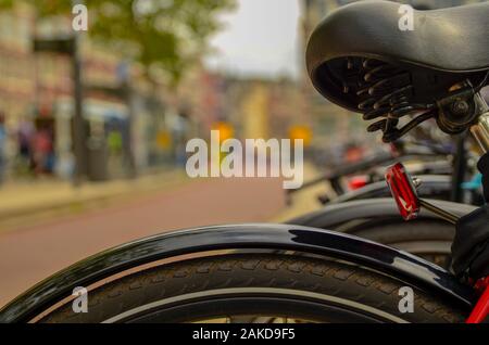 Amsterdam, Olanda, Agosto 2019.Un particolare punto di vista: dal telaio sfocata e la sella di una bicicletta parcheggiata possiamo vedere i ciclisti che passa sulla cycl Foto Stock