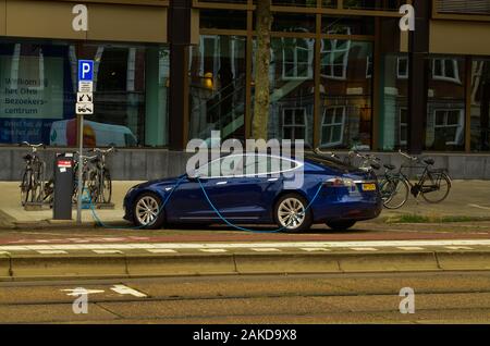 Amsterdam, Paesi Bassi, Agosto 2019. Un auto elettrica dal produttore Tesla. Essa è stata parcheggiata in corrispondenza di una stazione di carica. Il cavo blu è collegato Foto Stock