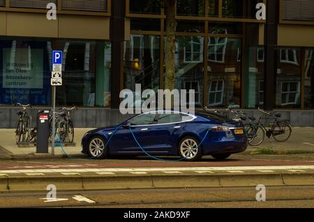 Amsterdam, Paesi Bassi, Agosto 2019. Un auto elettrica dal produttore Tesla. Essa è stata parcheggiata in corrispondenza di una stazione di carica. Il cavo blu è collegato Foto Stock