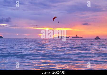 Il parasailing paracadute, battenti in luminoso Cielo di tramonto oltre la porpora acque del mare delle Andamane, Patong, Phuket, Tailandia Foto Stock