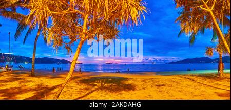 Panorama della spiaggia di sera attraverso la alberi tropicali in luci luminose, Patong, Phuket, Tailandia Foto Stock