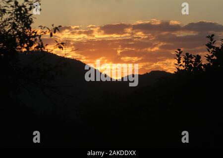 Sole che tramonta dietro le montagne Foto Stock