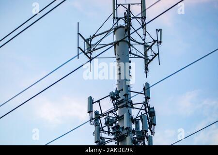 Un vicino la vista dettagliata di antenna multipla alloggiato su di un monopolo. Tettuccio di cavi attraversano una rete cellulare stazione base contro una luce blu cielo Foto Stock