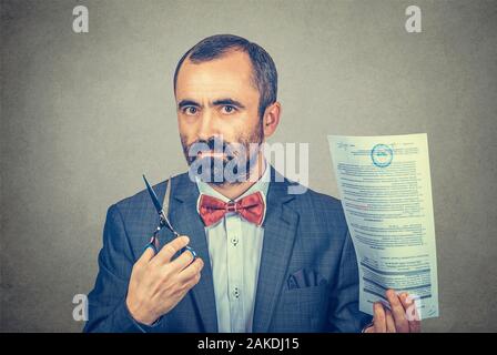 Ritratto di faccia stolid barbuto imprenditore in elegante giacca con red bow tie, tenendo le forbici e documento importante contratto nelle sue mani, ready t Foto Stock