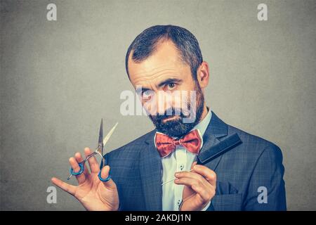 Parrucchiere barbuto, indossa una giacca elegante con red bow tie, posa con forbici e pettine. Elegante uomo adulto ritratto in studio, isolato a backg grigio Foto Stock