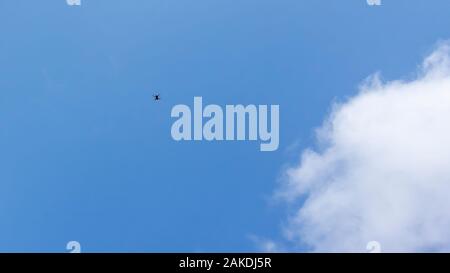 Un piccolo drone in alto nel cielo sopra la testa e con il bianco delle nuvole in background Foto Stock