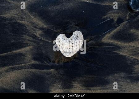 Bianco a forma di cuore sulla pietra di sabbia nera vulcanica. Foto Stock