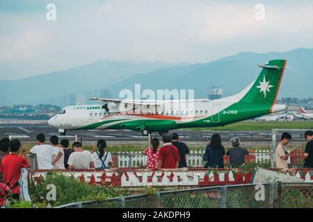 Un aereo UNI Air si allinea sulla pista all'aeroporto di Songshan, mentre una folla di persone guarda dall'esterno della recinzione Foto Stock