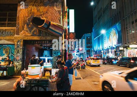 Un venditore di strada vende rinfreschi su un angolo di strada davanti ad una scarpa gigante è montato sulla parete del negozio di scarpe Macanna Foto Stock