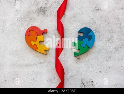 Puzzle multicolore in legno sotto forma di cuore rotto su sfondo grigio. Nastro rosso. Concetto valentines giorno, relazione. Spazio per il testo Foto Stock