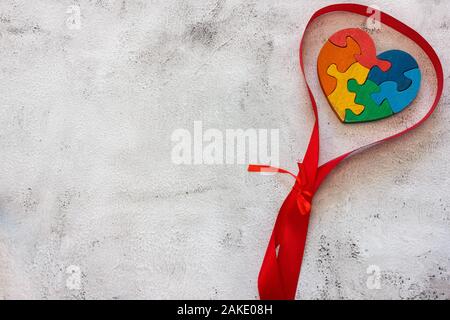 Puzzle multicolore in legno a forma di cuore su sfondo grigio. Concetto valentines giorno, relazione. Spazio per il testo Foto Stock