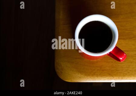 Red mug di caldo americano caffè nero sulla parte superiore del tavolo in legno con la luce del mattino al coffee shop. pausa caffè per rinfrescare nella lavorazione Foto Stock