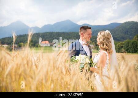 Lo sposo abbracci sposa teneramente nel campo di grano da qualche parte nella campagna slovena. Foto Stock