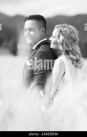 Sposi novelli abbracciando teneramente nel campo di grano da qualche parte nella campagna slovena. Caucasico romantico felice coppia giovane per celebrare il loro matrimonio Foto Stock