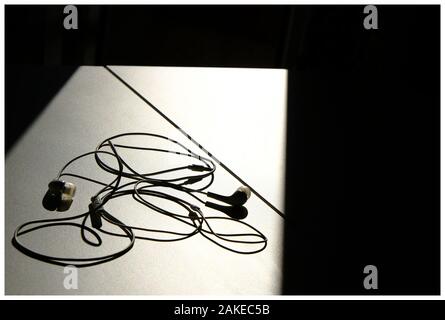 auricolari sdraiati in luce e ombra sul tavolo bianco Foto Stock