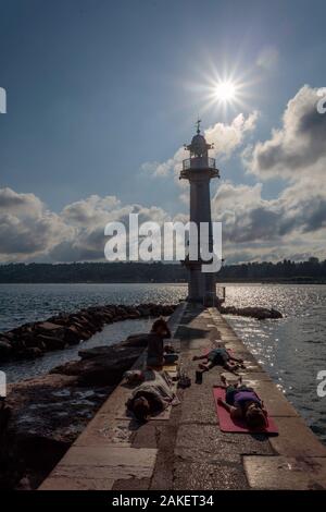 Quattro persone praticano lo yoga e la meditazione a Bains de Paquis accanto al faro. Lago Leman, Ginevra. Svizzera Foto Stock