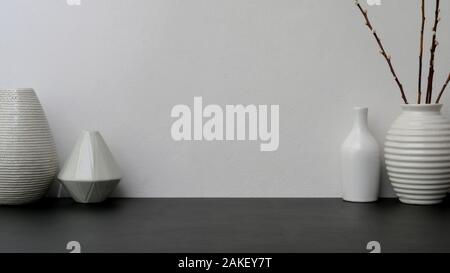 Vista ravvicinata della moderna area di lavoro con vaso in ceramica nera sulla scrivania con muro bianco sullo sfondo Foto Stock