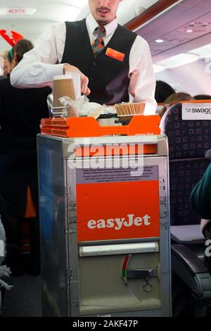 L'equipaggio di cabina / il servizio di steward serve bevande e spuntini ai passeggeri da un carrello durante un volo Easyjet su un aereo Airbus. (115) Foto Stock