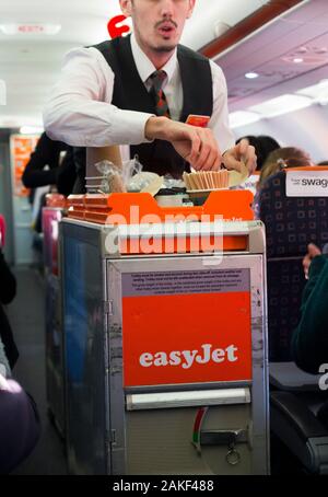 L'equipaggio di cabina / il servizio di steward serve bevande e spuntini ai passeggeri da un carrello durante un volo Easyjet su un aereo Airbus. (115) Foto Stock