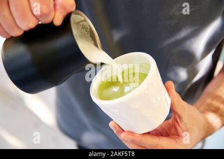 Barista maschio rendendo vegane matcha cappuccino con Latte di avena con latte art in outdoor cafe. Foto Stock