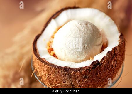 Porzione di deliziosi gelati con dadi e salsa di limone in dimezzato di noce di cocco. Servito in vetro frantumato con gusci di noce di cocco, su sfondo beige. Foto Stock