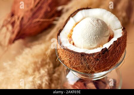 Porzione di deliziosi gelati con dadi e salsa di limone in dimezzato di noce di cocco. Servito in vetro frantumato con gusci di noce di cocco, su sfondo beige. Foto Stock