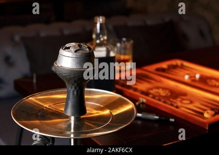 Hookah, bottiglia e bicchiere di whiskey, backgammon board sulla tabella nella barra di colore scuro. Concetto di insieme di riposo dopo la dura giornata. Foto Stock