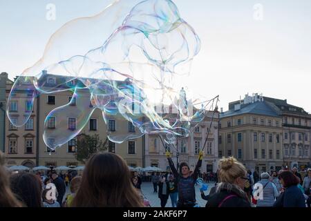 La gente guarda un uomo che crea bolle giganti nel Rynek Glowny (Piazza del mercato principale) nel centro di Cracovia (Cracovia), Polonia Foto Stock