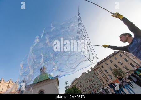 La gente guarda un uomo che crea bolle giganti nel Rynek Glowny (Piazza del mercato principale) nel centro di Cracovia (Cracovia), Polonia Foto Stock