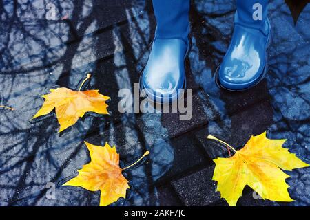 Donna con blu stivali da pioggia salta in una pozza sul piovosa giornata d'autunno Foto Stock