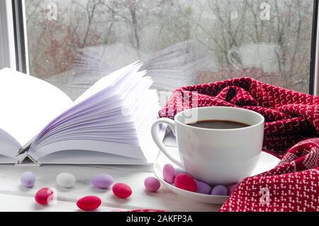 Accogliente casa ancora in vita: la tazza di caffè caldo e libro aperto con caldi plaid sul davanzale contro la neve paesaggio al di fuori Foto Stock