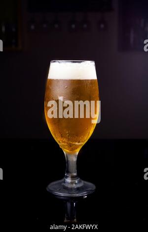 Di ghiaccio freddo bicchiere pieno di birra, con chopp pilsen su uno sfondo scuro in un pub Foto Stock