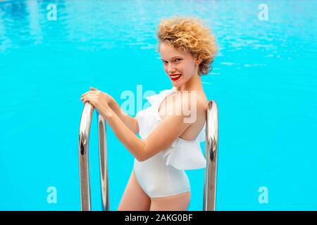 Bella rossa (zenzero) donna seduta e sorridente a bordo piscina in estate il giorno. Estate, felicità, relax, benessere, concetto di ricreazione Foto Stock