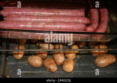 Le salsicce vengono cotti in forno contro lo sfondo di patate fritte in fondo c Foto Stock