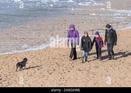 Una famiglia e il loro cane godendo di una passeggiata lungo Fistral Beach in Newquay in Cornovaglia. Foto Stock
