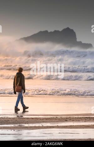 Un giovane uomo che cammina lungo il litorale verso Goose isola al largo della costa di Newquay in Cornovaglia. Foto Stock