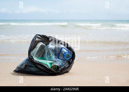 Vista dettagliata del grigio di un sacchetto di plastica con rifiuti raccolti sulla sabbia di una spiaggia solitaria, accanto all'acqua, in background Foto Stock