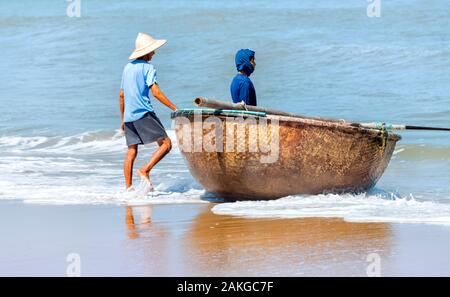 Due pescatori vietnamiti si sono quasi impegnati a prendere la loro barca di coracle fuori dal mare Foto Stock