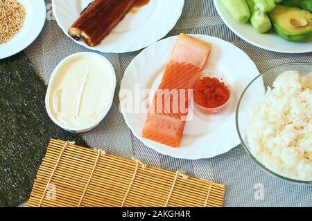 In casa rotoli di sushi preparato. Ingredienti tradizionali prodotti prodotto alimentare sulla home tavolo da cucina pronti per essere preparati. Cibo asiatico sfondo Foto Stock