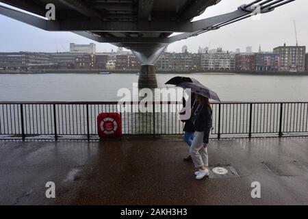 Londra, Regno Unito, 9 gennaio 2020, Meteo. Pomeriggio buio in città con la pioggia intensa. Una coppia che tiene gli ombrelli che cammina sotto il Millennium Bridge. Foto Stock