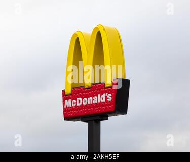Junction One Retail Park, Rugby, Warwickshire, Regno Unito: Il ristorante McDonalds firma su una pole nera contro un cielo grigio chiaro. Foto Stock