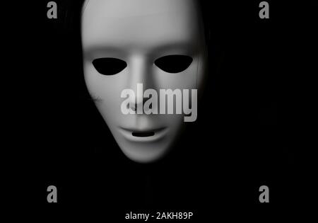Maschera bianca spaventosa al buio. Ragazzo Spooky in mascherata bianca. Occhi neri e invisibili. Capelli neri. Stile Halloween. Foto Stock