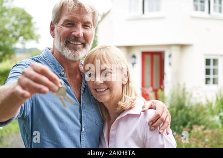 Ritratto Di Coppia Matura In Piedi In Giardino Davanti A Dream Home In Campagna Holding Keysgature Foto Stock