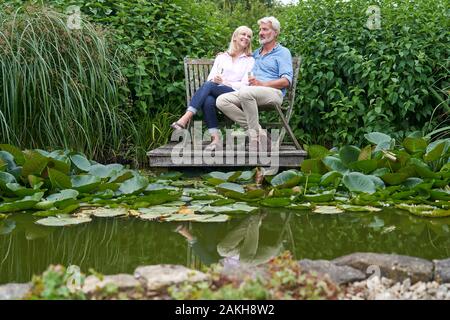 Coppia Matura celebrando con Champagne seduti su sedie sul pontile in legno sul Lago di Garda Foto Stock